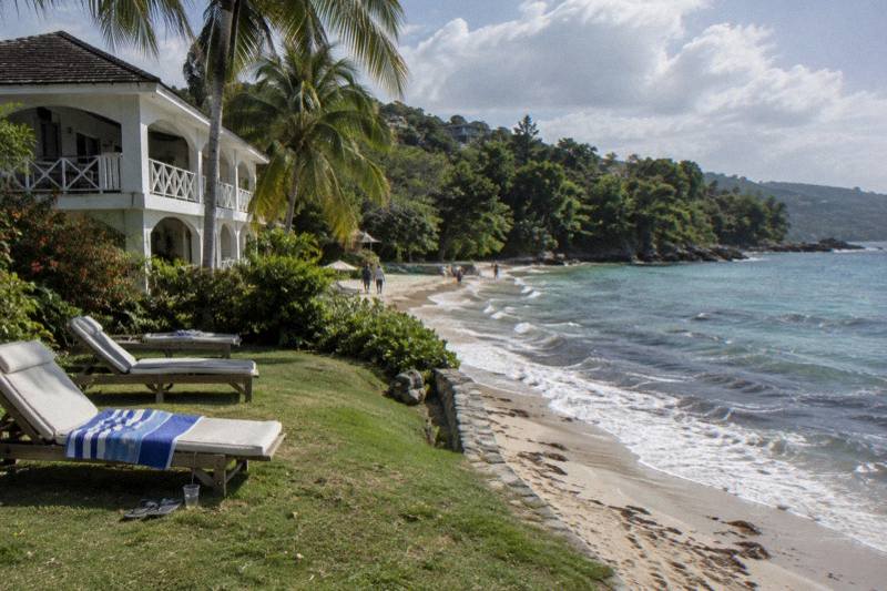 Whitewashed oceanfront inn with loungers on a lawn above the beach