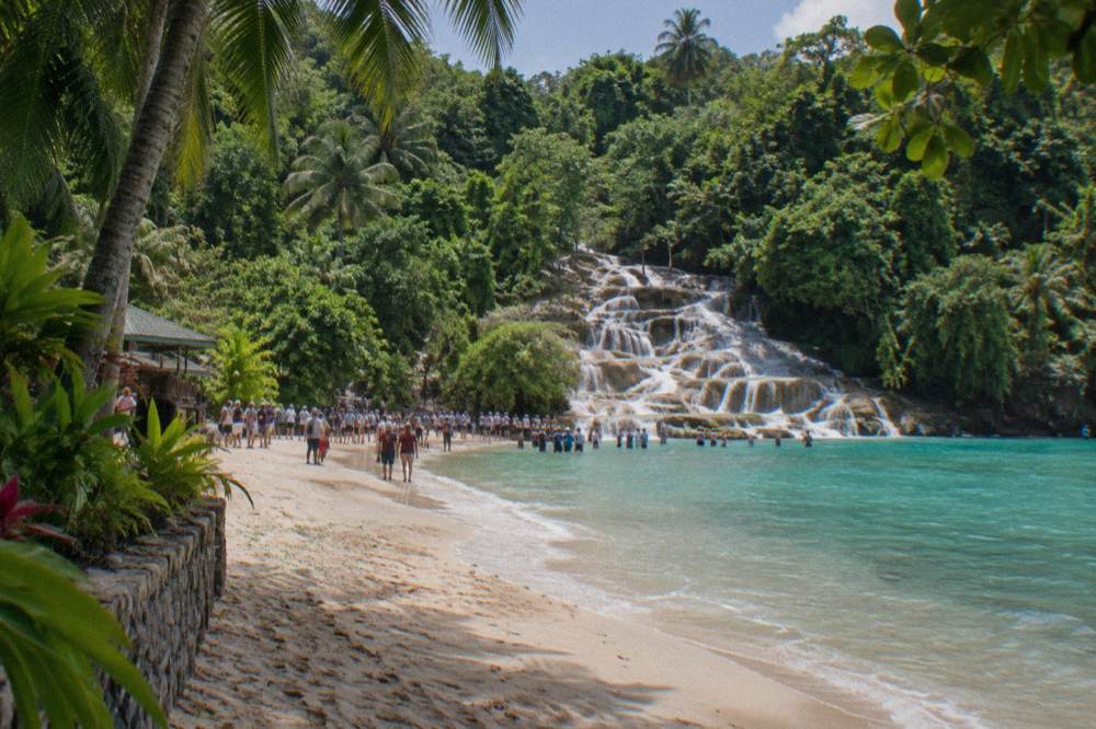 Calm sandy beach at the base of the waterfall with calm turquoise water
