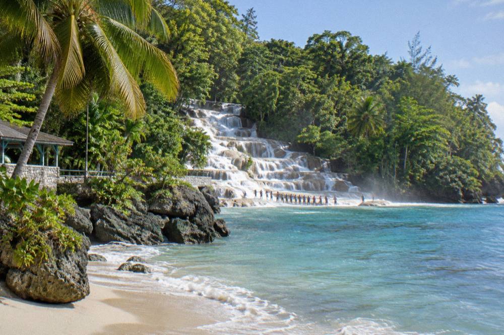 Visitors forming a chain in the shallow water at the base of a wide terraced waterfall