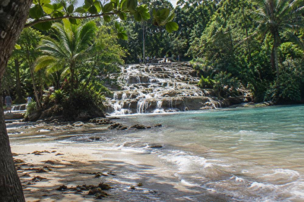 Sandy beach at the foot of a waterfall where river water meets calm turquoise Caribbean sea