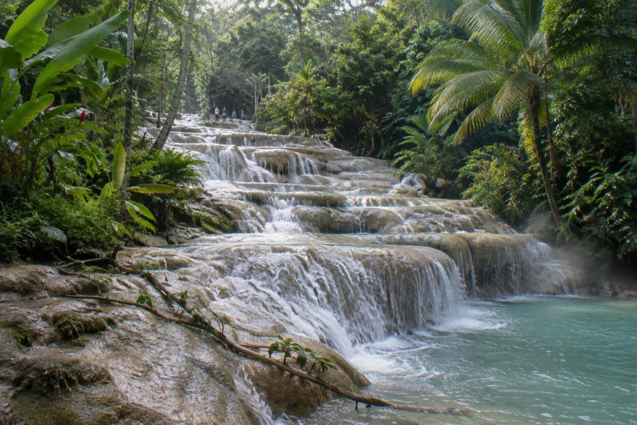 Terraced waterfall cascading over pale rock steps into a natural pool edged with green tropical foliage