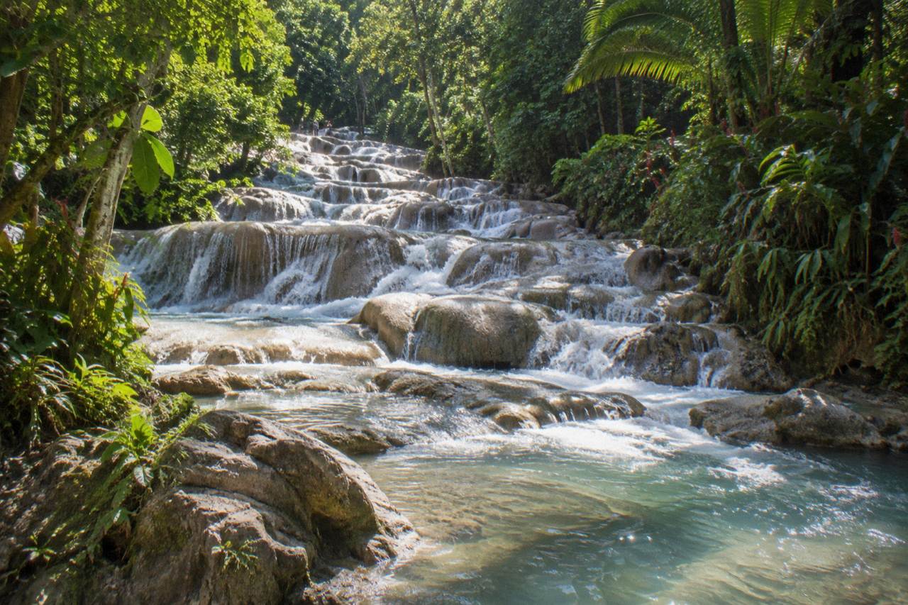 Terraced limestone steps of a waterfall cascading into a rocky river channel with tropical forest on both sides