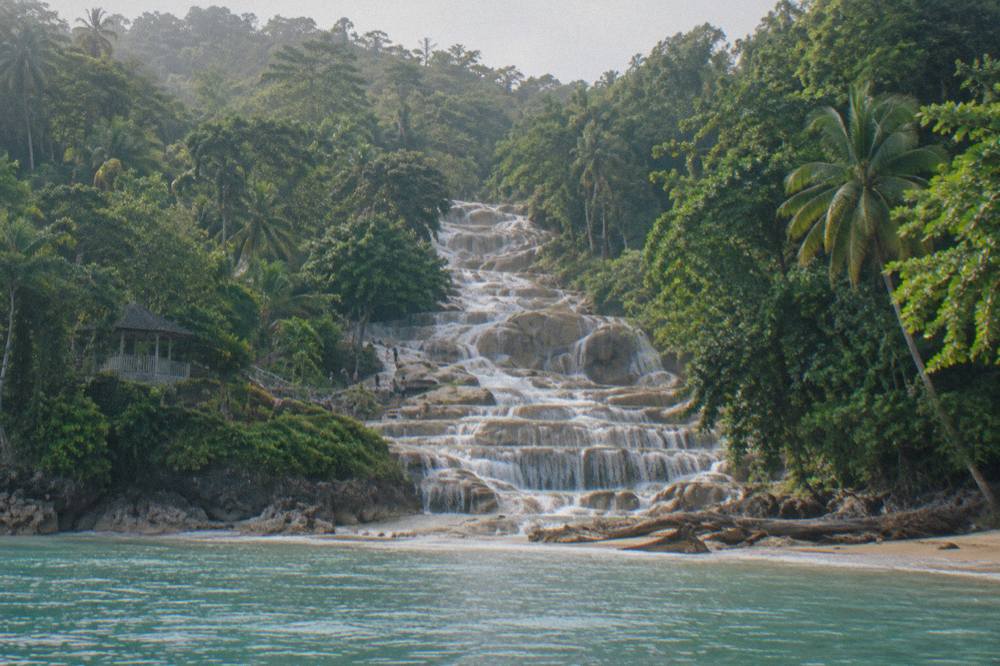 Wide waterfall of stepped limestone terraces spilling into a small sandy beach between green hills