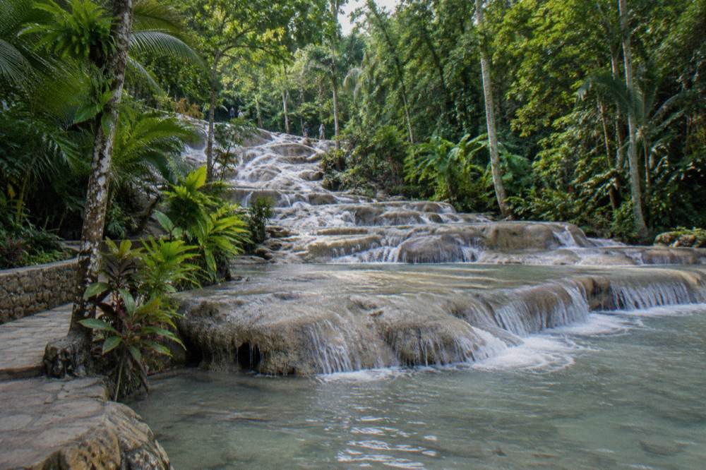 Smooth limestone terraces of the waterfall with shallow pools and tropical trees on both banks