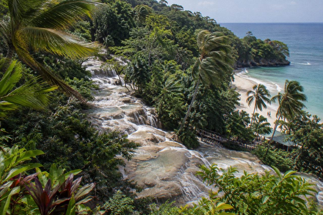 Terraced limestone steps of a wide waterfall cascading into a Caribbean beach cove