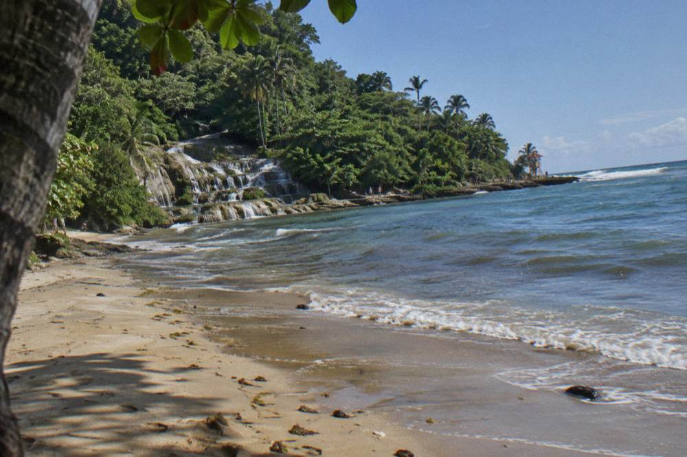 Terraced falls stepping down to sand and calm Caribbean water, a distant lifeguard tower and drying footprints