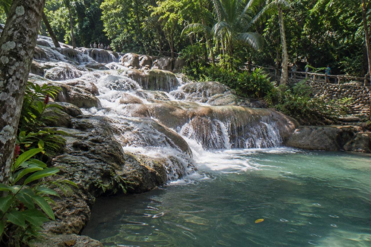 Terraced limestone steps of a tall waterfall cascading into a natural pool surrounded by green tropical forest