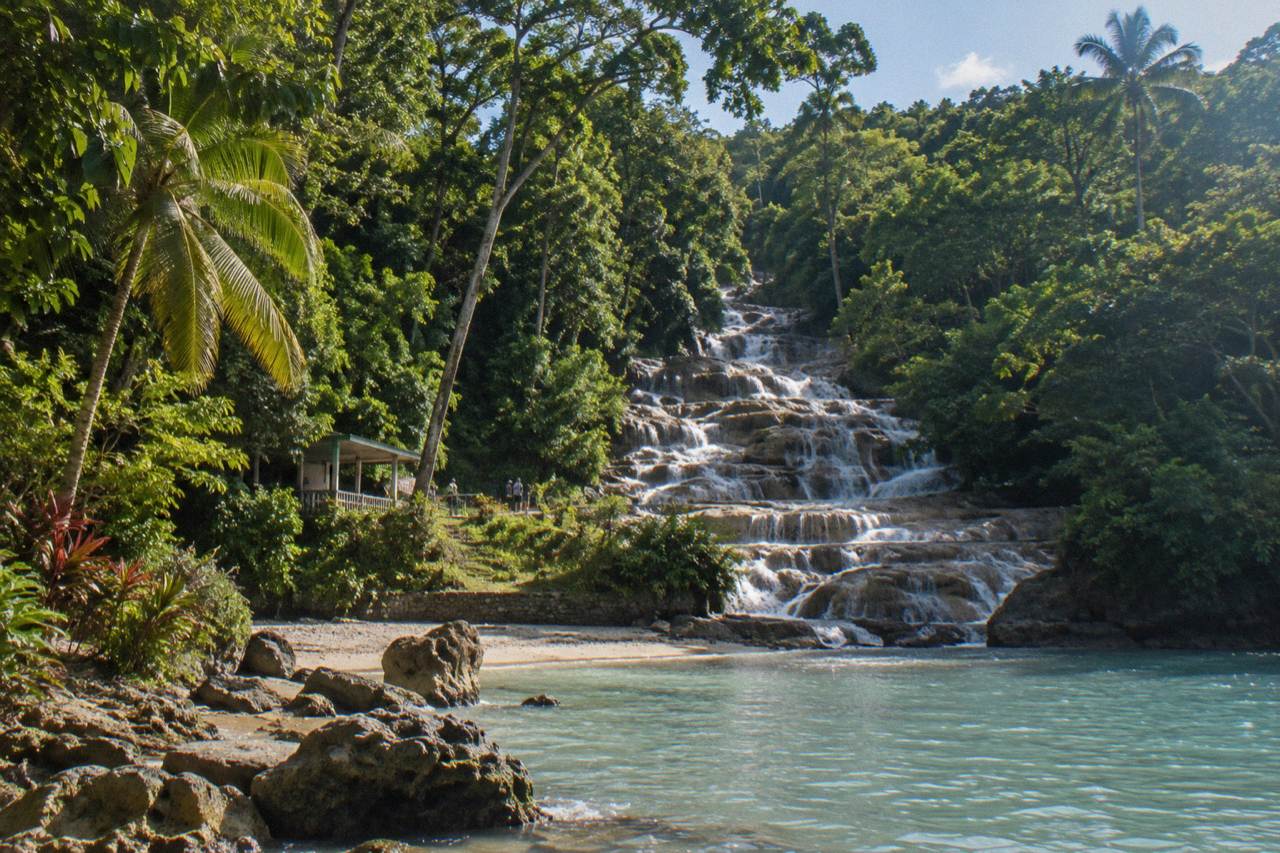 Terraced waterfall cascading through a green jungle setting toward a small beach and the sea