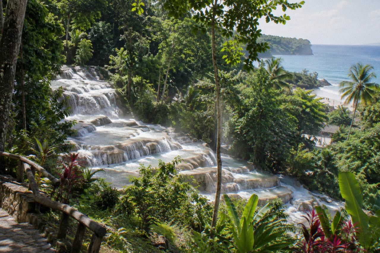 Terraced waterfall cascading through a green tropical gorge toward a sandy beach