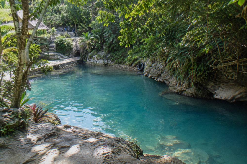 Calm turquoise pool of water framed by limestone rocks and overhanging tropical trees