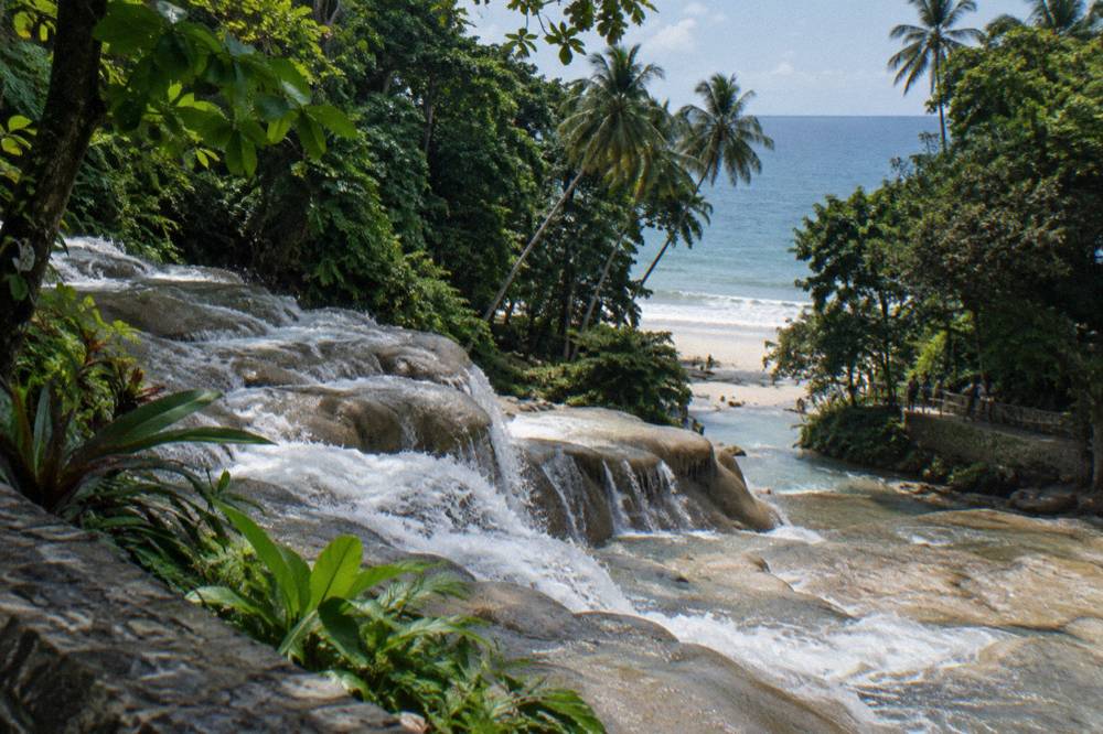 Waterfall cascading down smooth limestone terraces toward a beach and the sea beyond