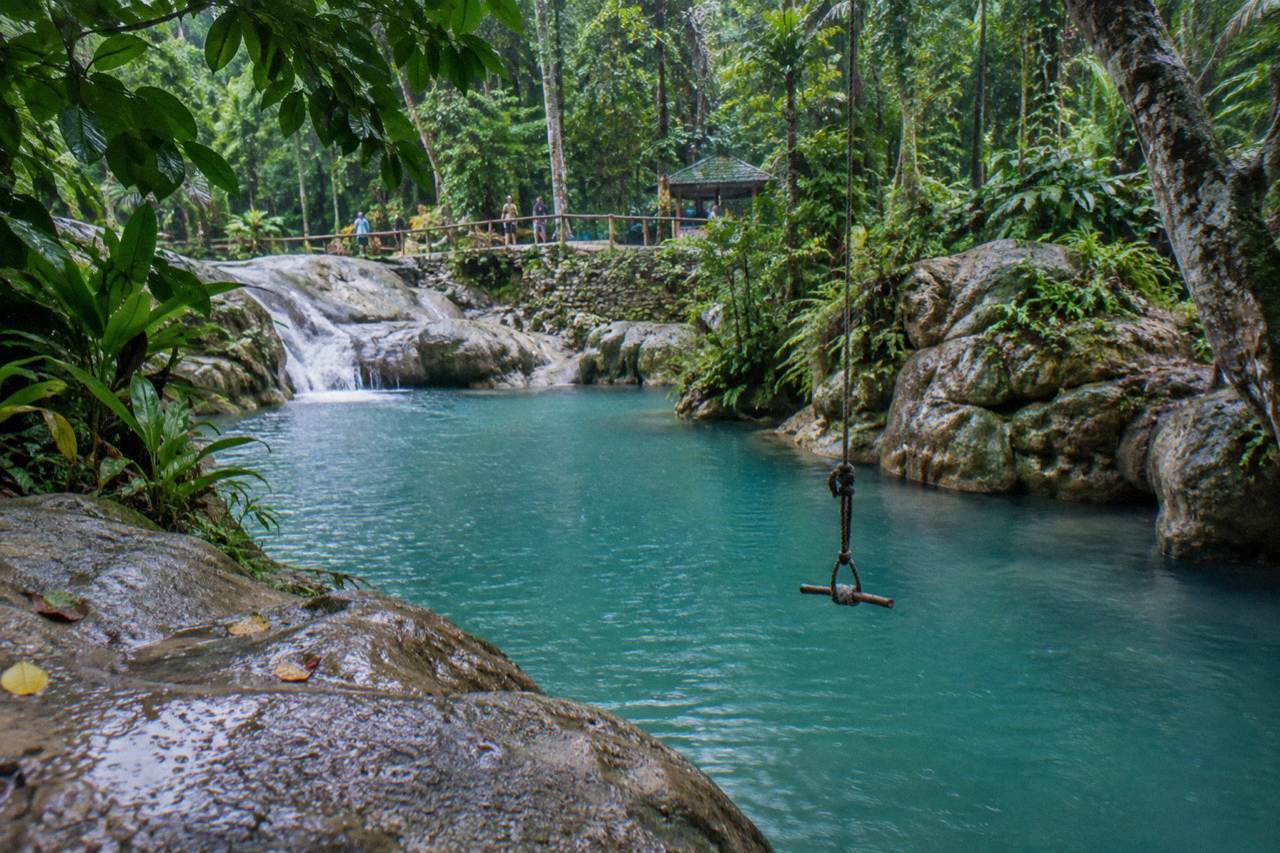 Turquoise water pooling among rocks at a Jamaican waterfall surrounded by dense green forest