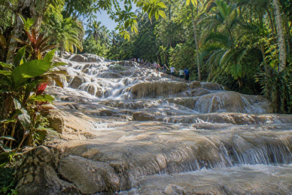 Guided group forming a human chain while climbing a wide stepped waterfall
