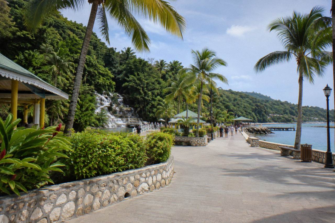 Sunny clean paved promenade with palms by a calm harbour, distant tourists and a police car parked far away.