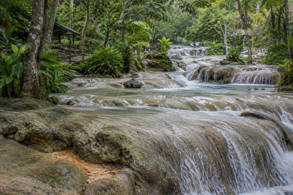 Terraced waterfall steps with water flowing over smooth limestone ledges surrounded by green forest