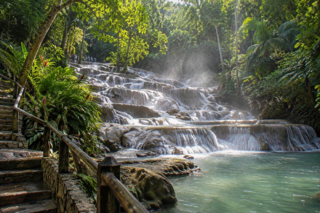 Waterfall cascading down terraced limestone steps toward a tropical pool