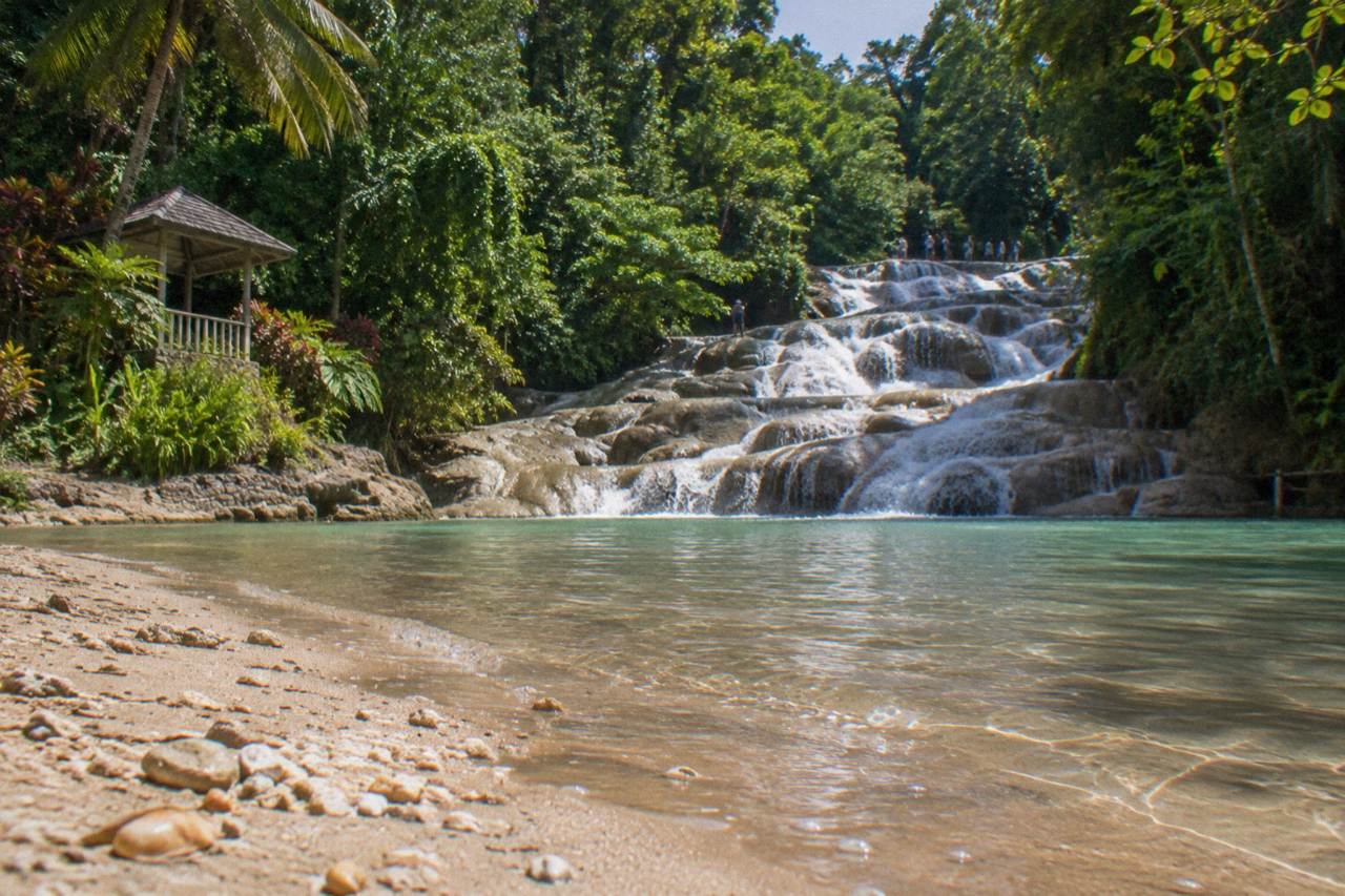 Terraced waterfall cascading through a green tropical gorge toward a Caribbean beach