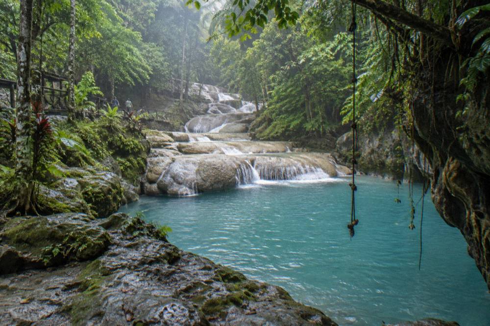 Turquoise swim hole surrounded by rocky ledges and dense jungle foliage