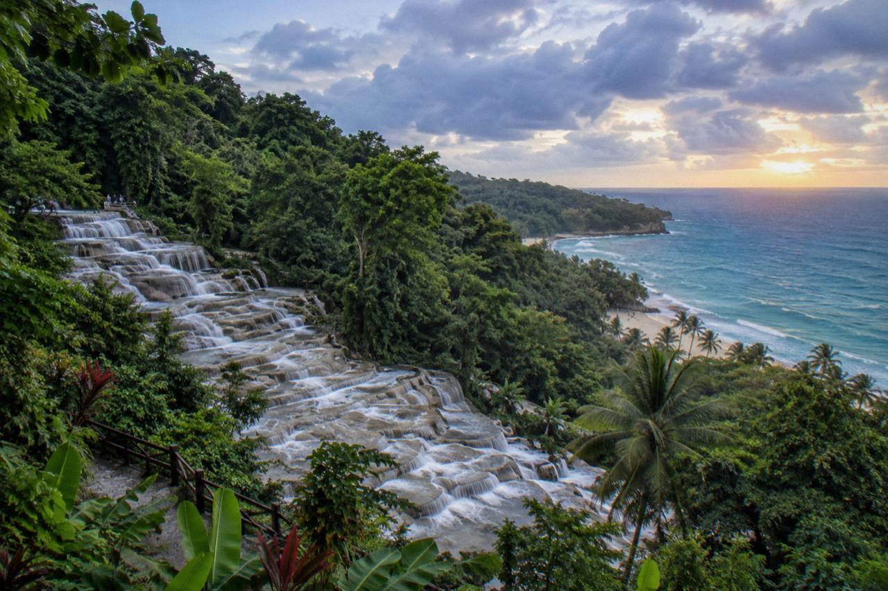 Wide terraced waterfall cascading through tropical forest toward a beach and the sea