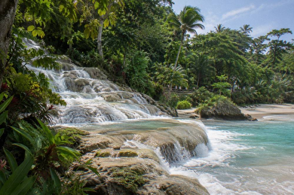 Turquoise water spilling over stone terraces at a tropical waterfall into a sandy cove