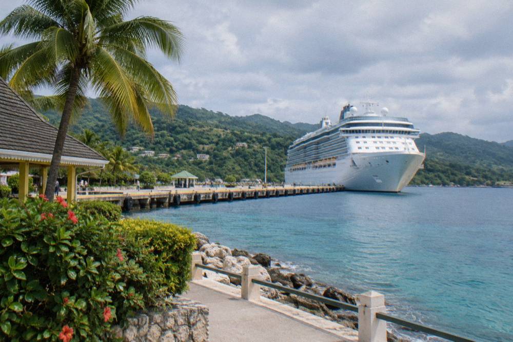 Cruise ship docked at a small Caribbean port town beside forested hills