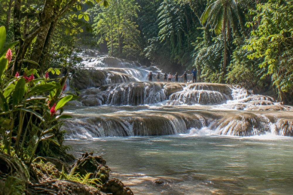 Line of visitors holding hands in a waterfall channel as a guide points the way