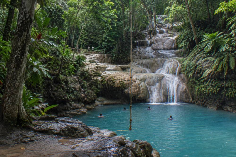 Swimmers in a blue natural pool below a small jungle waterfall