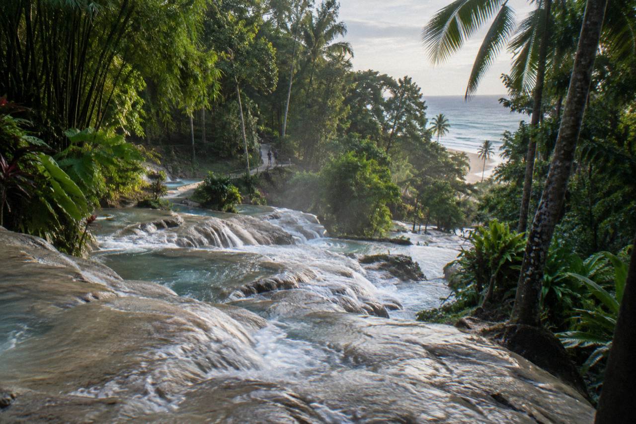 Terraced waterfall cascading through a green tropical gorge toward a sandy beach