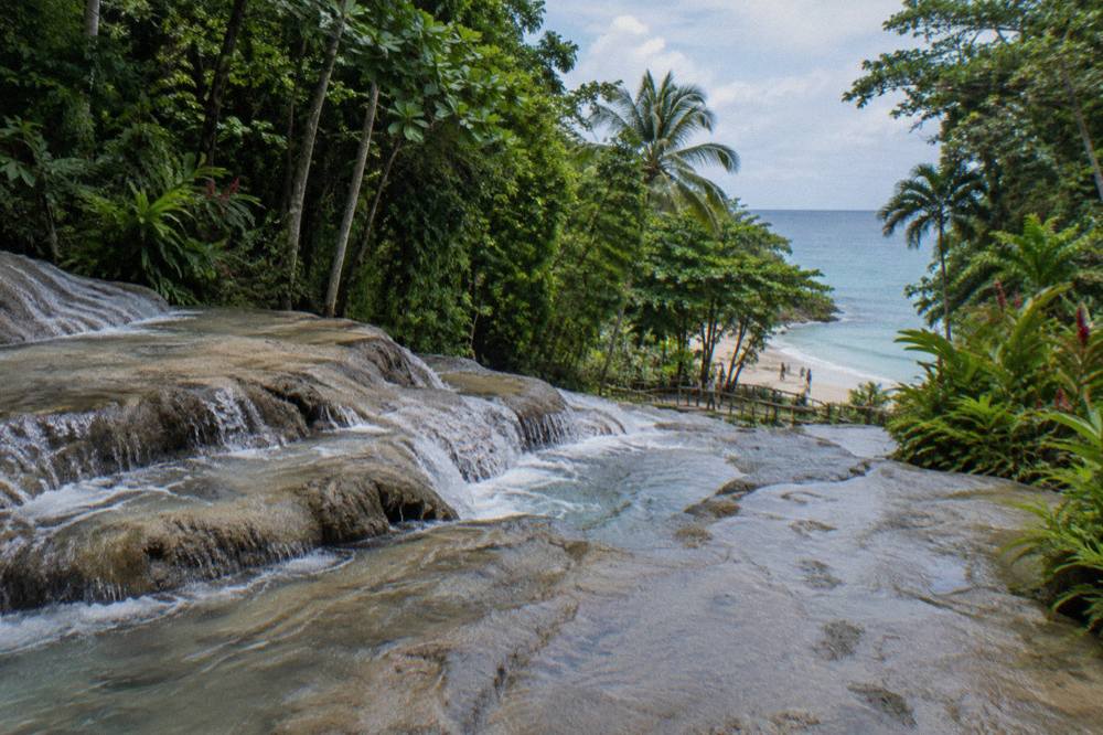 Waterfall terraces descending through tropical forest toward a sandy beach