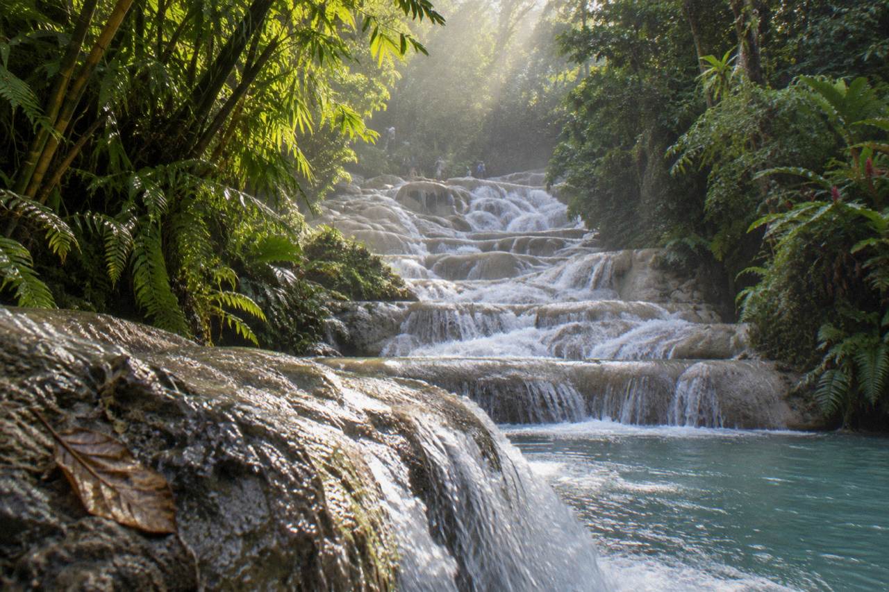 Terraced waterfall cascading through a green Jamaican gorge toward the sea
