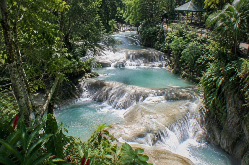 Turquoise water spilling over stepped limestone rock ledges in a tropical gorge