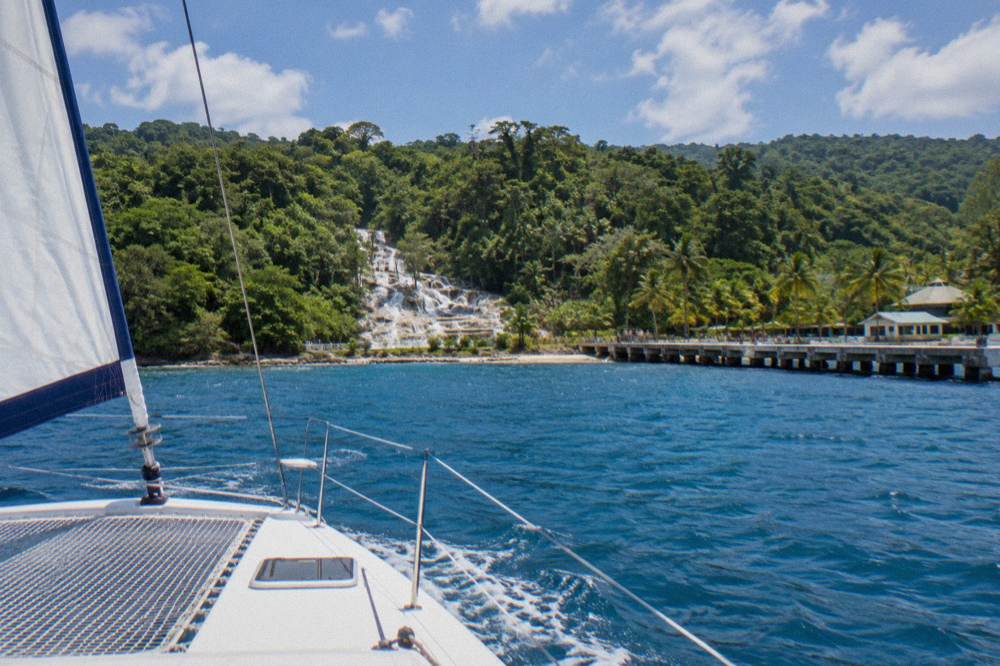 A sailing catamaran on open water near a green coastline