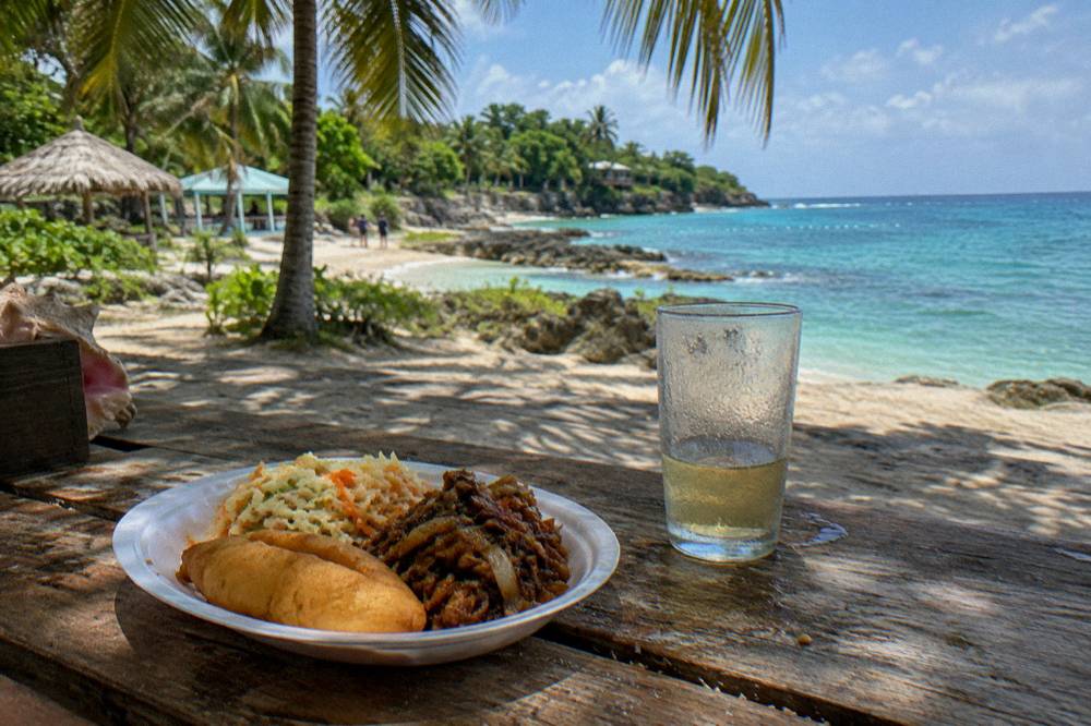 Plates of tapas food on a table under palm shade beside the sea