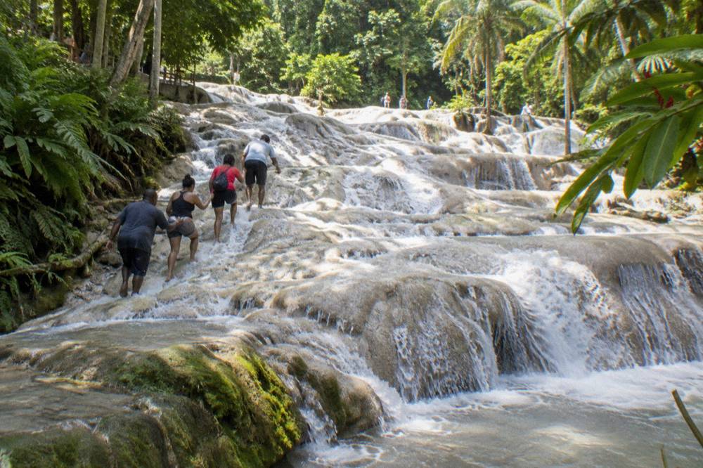 Guided group holding hands in a chain while climbing a stepped limestone waterfall