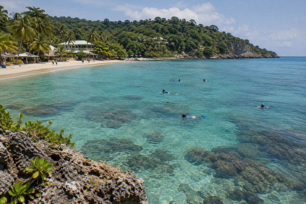 Snorkelers in calm shallow water above a coral reef on a sunny day