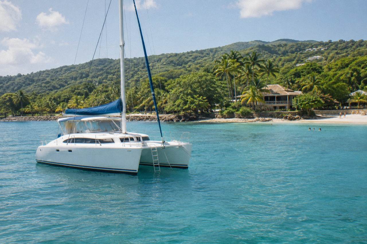 A catamaran anchored in clear Caribbean water below a green coastline near Ocho Rios