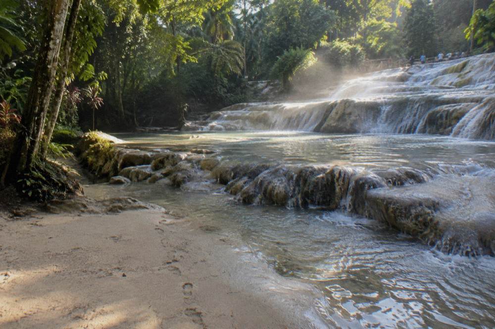First light on empty terraced falls, water sheeting over pale steps, mist rising, one trail of footprints