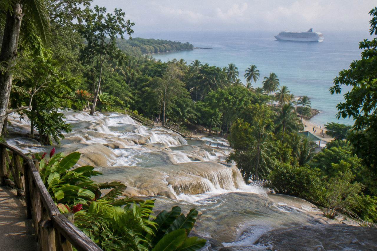 Waterfall terraces descending toward a beach with a cruise ship anchored offshore