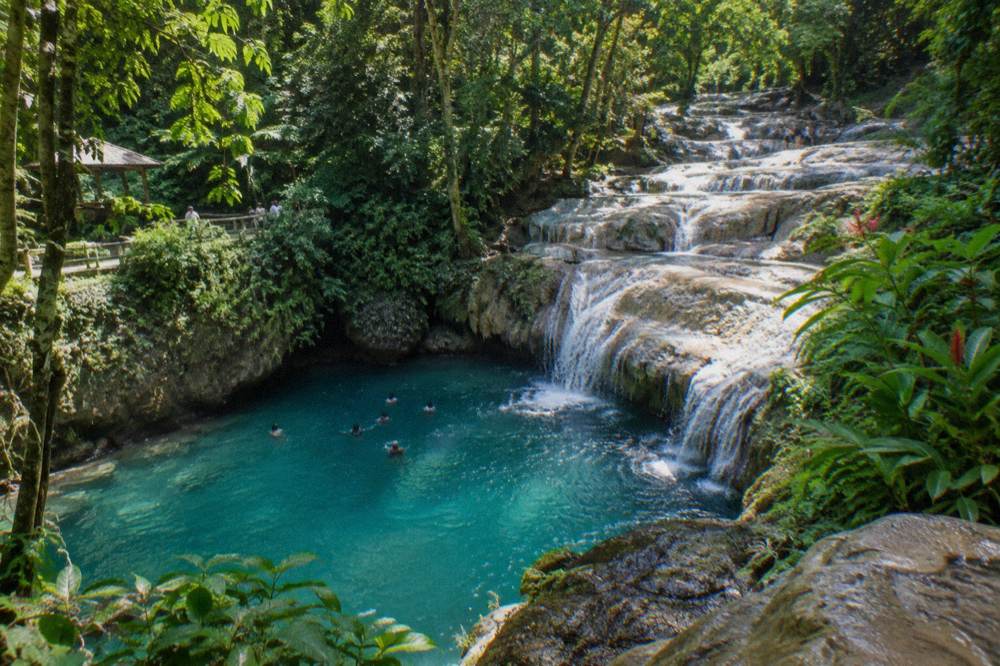 Swimmers in a turquoise pool at the base of a jungle waterfall