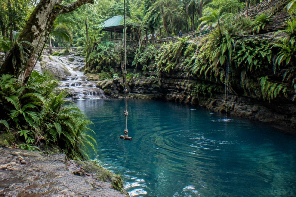 Rope swing over a deep blue swimming hole surrounded by limestone rocks
