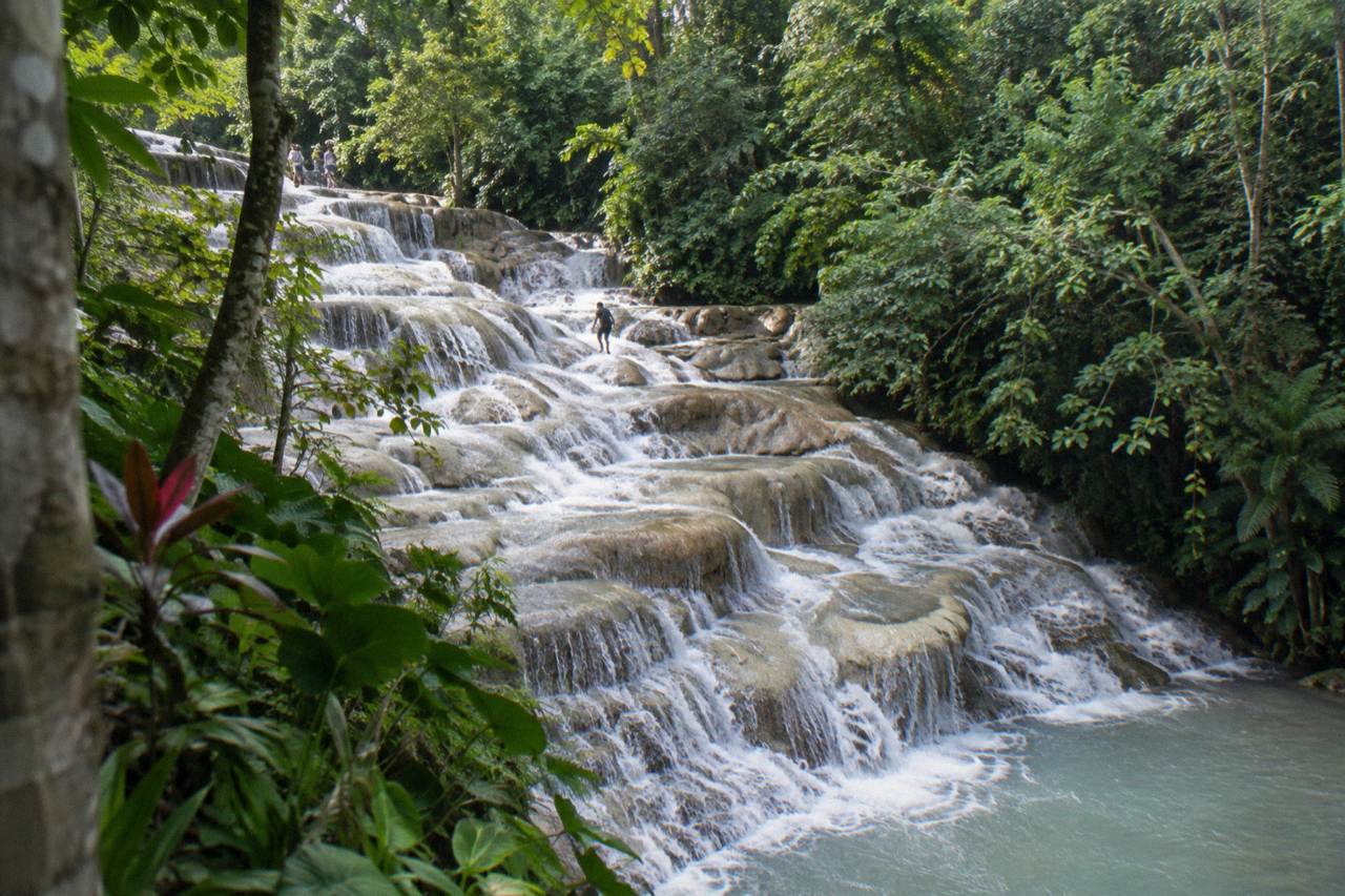 Waterfall terraces cascading through a green tropical gorge toward the sea