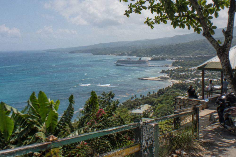 Morning from a coastal overlook, pale turquoise sea on one side, forested hills and valley haze on the other