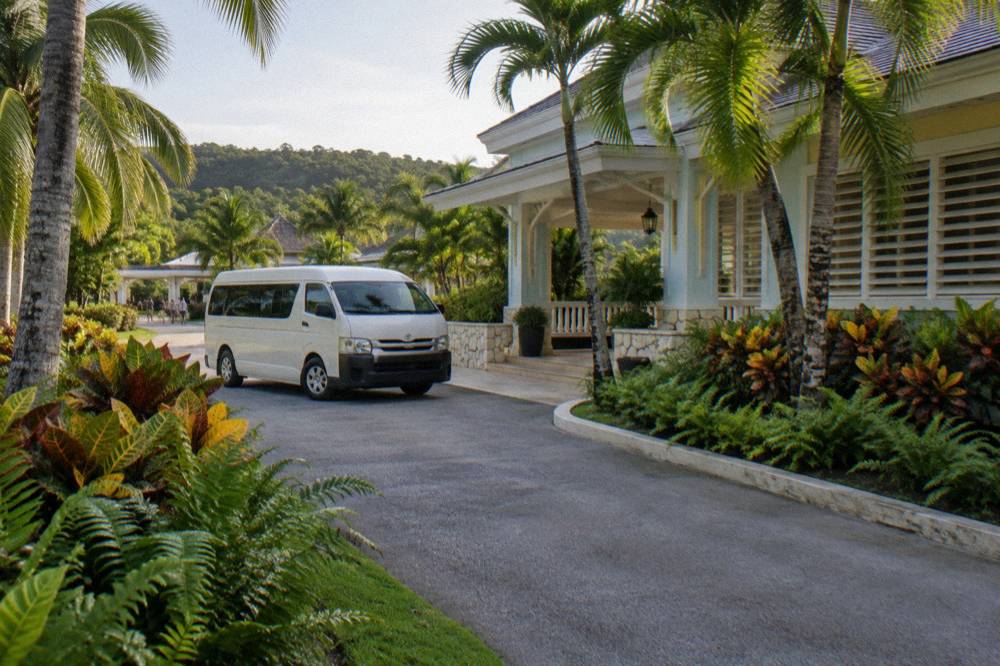 Resort entrance with a tour minivan waiting on a driveway lined with tropical plants
