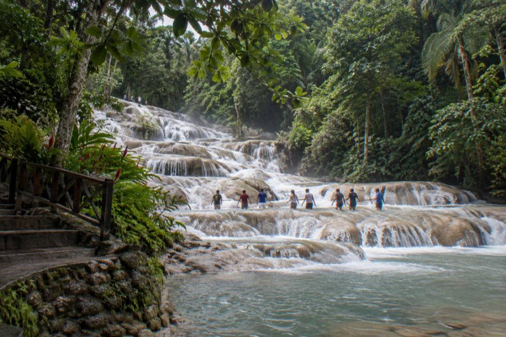 Visitors forming a chain while wading up shallow water steps of the waterfall