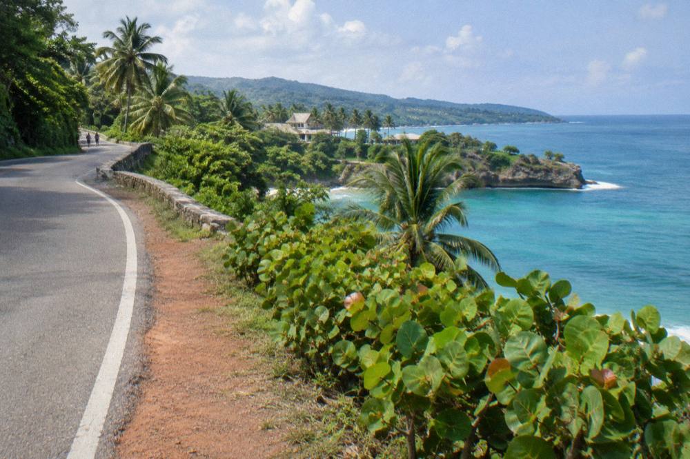 Coastal road curving along a shoreline with forested hills and calm sea