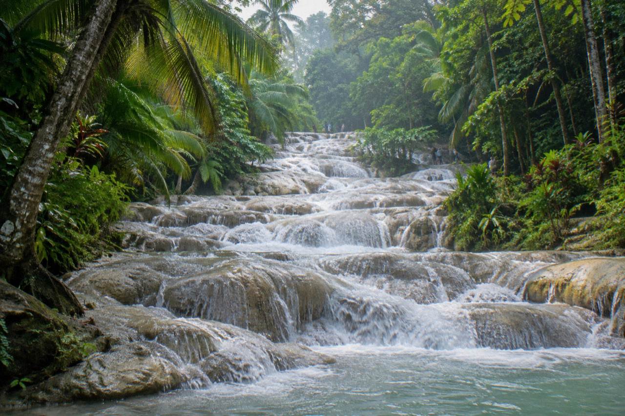 Terraced limestone steps of a waterfall cascading into a rocky river channel surrounded by tropical forest