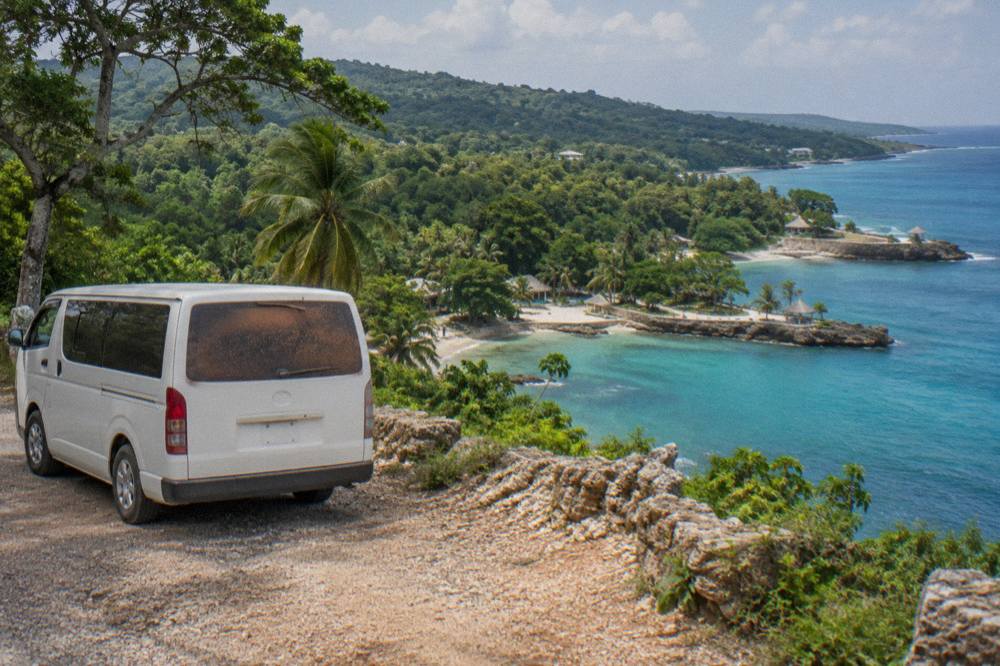 Private tour van parked on a coastal road above a turquoise bay