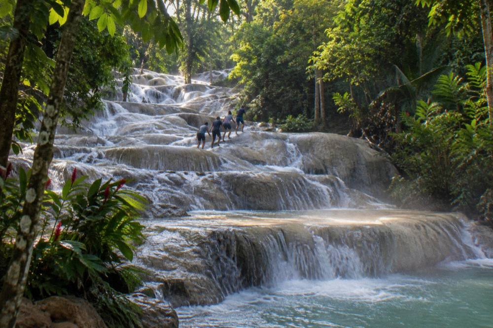 Small group of visitors forming a chain while climbing a terraced waterfall