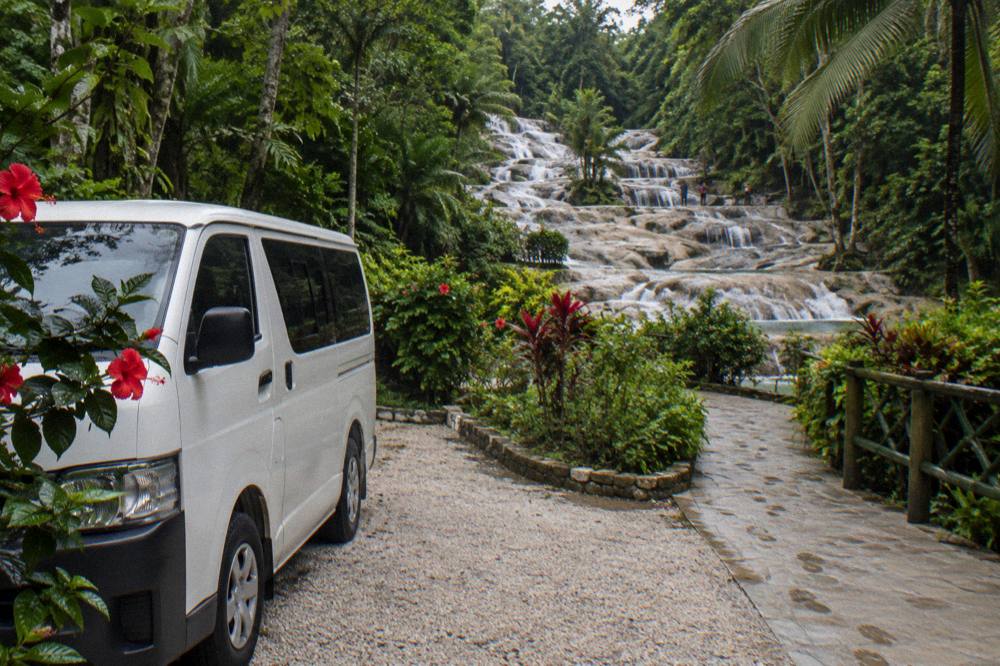 Tour vehicle waiting beside a tropical garden path near the falls