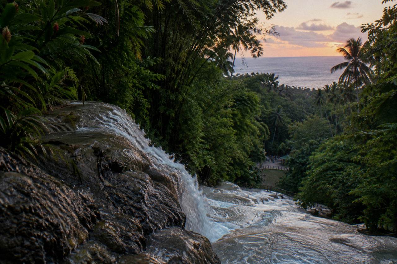 Terraced waterfall cascading through a green tropical gorge toward the sea